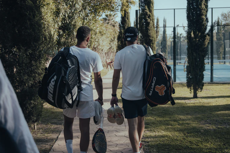 Two players walking to the courts with tennis bags at the Aurora Tennis Camp