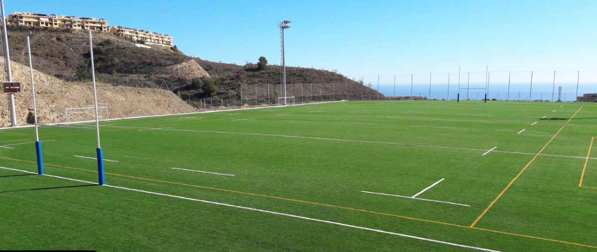 Empty rugby pitch with goalposts, hillside surroundings and a sea view